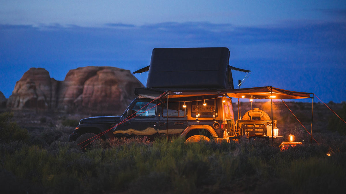 A lit campsite beside a four-wheel drive and rooftop tent at dusk